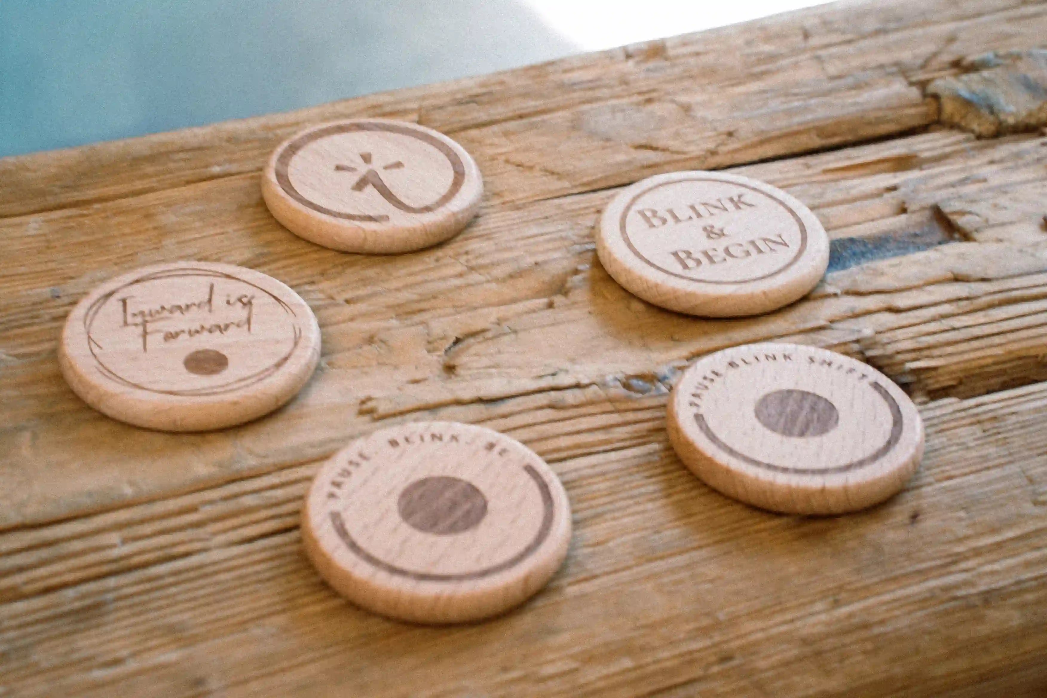 Five wooden blink tokens with engraved text on a wooden surface.