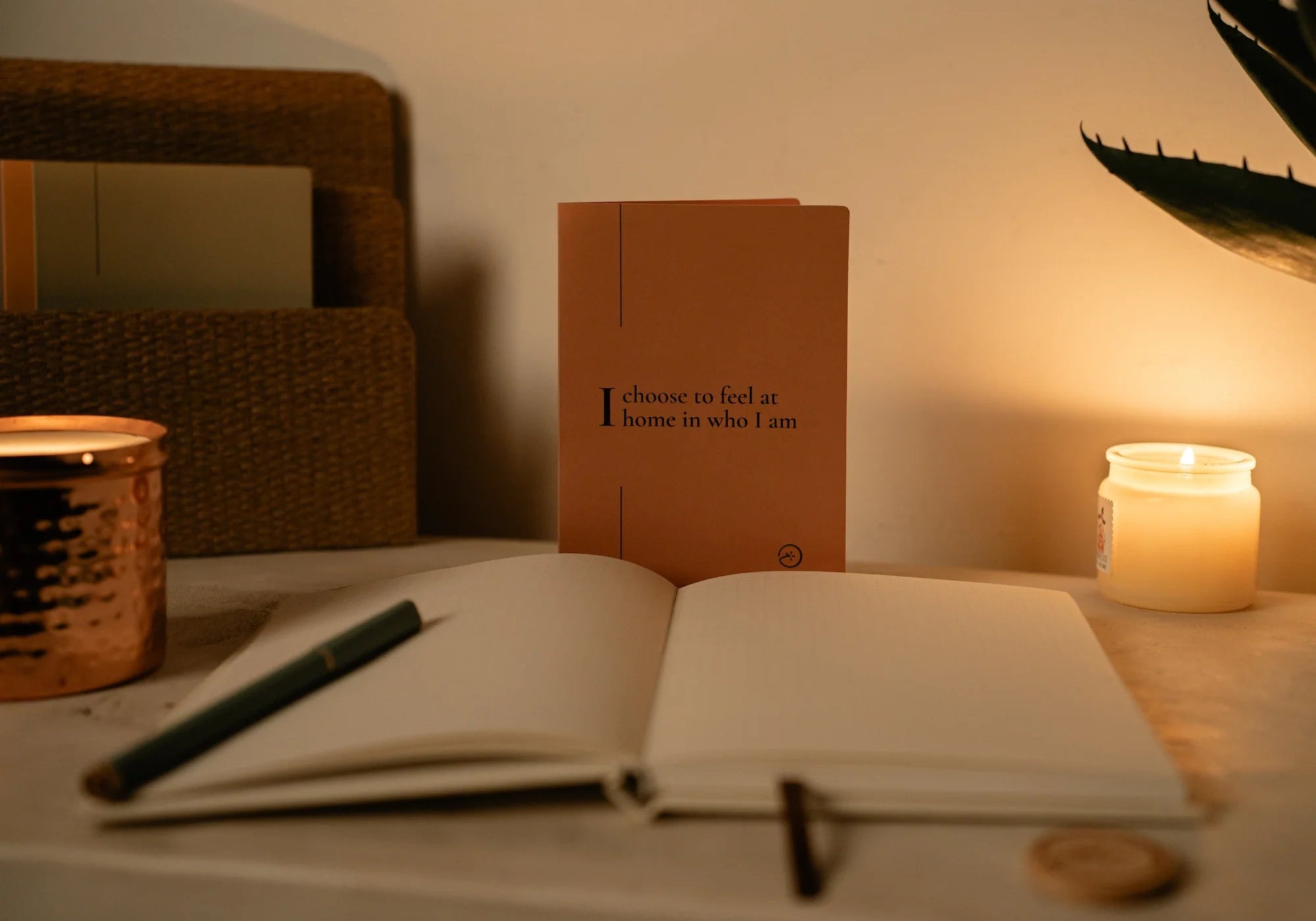 Open notebook with pen, candle, and plant on a table in warm lighting with a blink card